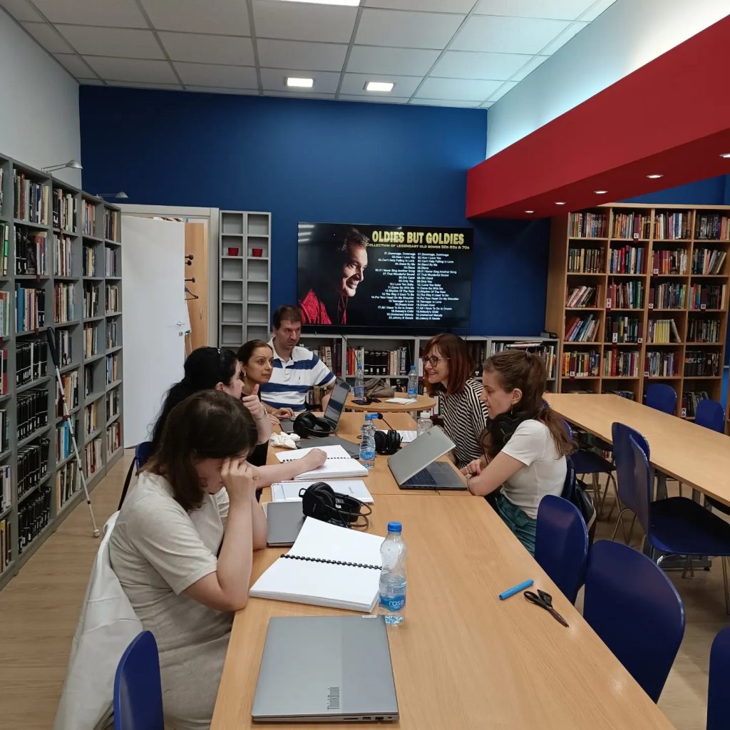 Učesnici obuke za dugačkim stolom koriste laptopove i slušalice za rad.